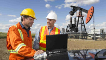 A royalty free image from the oil industry of two oil workers using a laptop in front of a pumpjack
