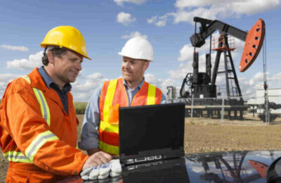 A royalty free image from the oil industry of two oil workers using a laptop in front of a pumpjack